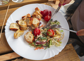 Woman eating grilled chicken and vegetable salad. Female hands with fork and knife, delicious food from barbecue.