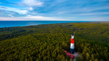 Aerial landscape of the lush green forest in a sunny day. Sea in the background. Bird's eye view of the lighthouse.