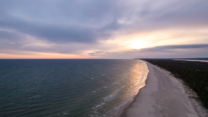 Landscape of the sandy beach during cloudy evening. Aerial view of the pine forest. Rays of the sun on the water.