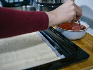 Unrecognizable caucasian woman's hand scooping fried tomato with spoon to spoon on top of pizza dough