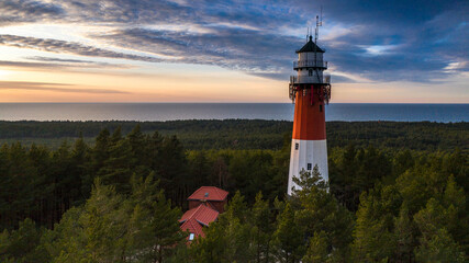 Aerial view of the lighthouse during sunset. Orange sky, dark clouds. Sea in the background.