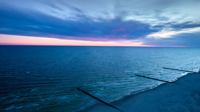 Sea after sunset, orange sky and dark clouds. View of the wooden breakwater. 