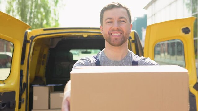 The courier delivers the parcel and hand it to the client. Portrait of a courier holding a parcel, a yellow car in the background