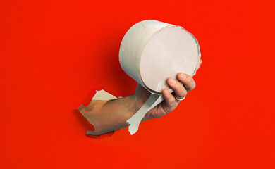 Hand hold a toilet paper roll in hand through torn red paper background