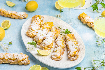 Eclairs with lemon curd topping on serving plate with glass of limoncello on a light background, concept of Italian and French cuisine, top view
