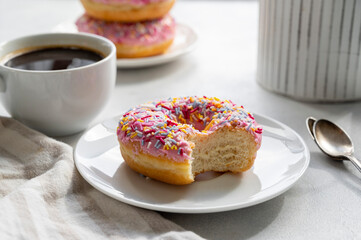 Pink donut with sprinkles and coffee cup for breakfast