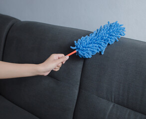 Hand using blue microfiber duster cleaning the sofa.
