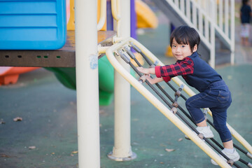 Little boy climbing rope on outdoor playground.
