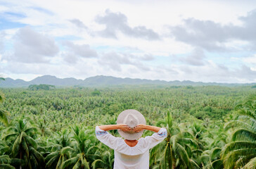 Tropical vacation. Young woman  in hat enjoying the view of beautiful coconut palms plantation.
