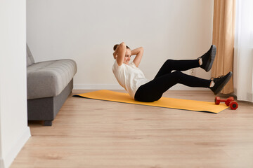 Side view portrait of sporty active woman doing cross training bicycle crunches trains leg muscles and abs, athlete conducts daily training on a mat in the room.