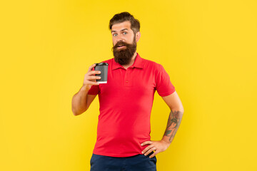 Surprised man in casual red tshirt holding disposable cup with arm akimbo, takeaway coffee