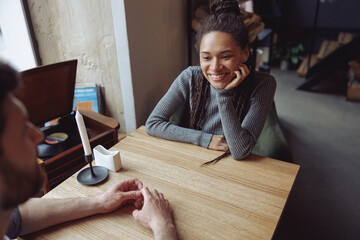Fototapeta na wymiar Beautiful young woman in love looking at man while sitting at table in cafe. Date. Mixed-race couple