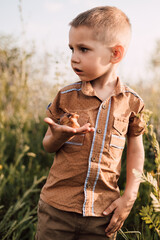 A little boy stands in the grass in nature and holds a snail in his hand