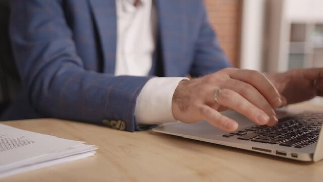 Close-up: a young man is typing something on a laptop. Then someone gives sheets of paper with reports, but the man pushes them away and continues typing. Slow motion 4k footage