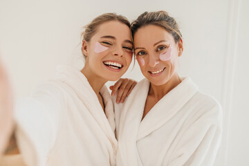 Happy caucasian mother with daughter wearing hydrogel patches smiling looking at camera on white...