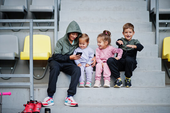 Four cuttie kids sitting on sport area and looking at mobile phone.