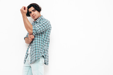 Portrait of handsome confident model. Sexy stylish man dressed in checkered shirt and jeans. Fashion hipster male posing near white wall in studio. Isolated