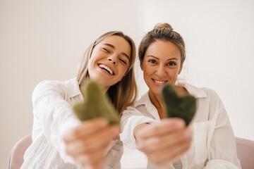 Positive young caucasian women in shirts holding gouache scraper on white background. Blondes wear good mood look at camera. Home spa concept