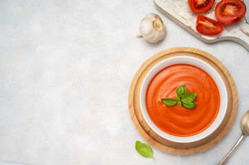 Tomato soup with fresh basil in orange bowl. Bright background. Healthy food concept. Copy space