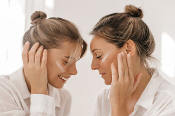 Close-up in profile of two caucasian ladies of different ages with closed eyes on white background....