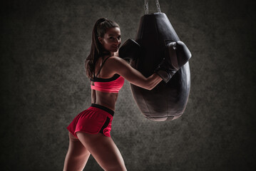 Athletic woman in red shorts and top posing near the bag. Boxing and mixed martial arts concept.