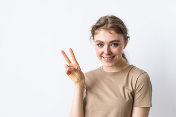 Young woman having fun, showing v-sign over eye and winking, smiling sassy at camera, being in good and positive mood, standing over white background