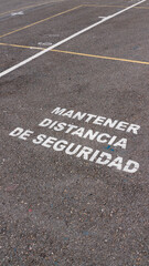 Cartel de "mantener distancia de seguridad" pintado con pintura blanca en suelo de asfalto