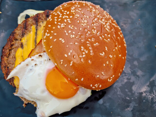 Fast food cheeseburger sandwich with a round bread bun, served with a fried egg and bacon.