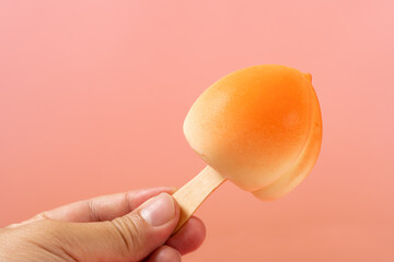 hand holding a peach shape popsicle on pink background
