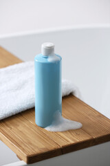 Bottle of bubble bath with foam and towel on tub in bathroom