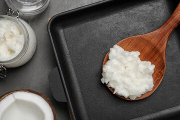 Baking dish with coconut oil and wooden spoon on grey table, flat lay