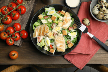 Delicious Caesar salad in bowl on wooden table, flat lay
