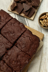 Delicious freshly baked brownies, walnuts and pieces of chocolate on white wooden table, flat lay