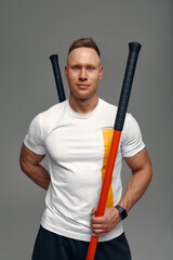 A fighter in white t-shirt and black shorts, stands in a fighting artificially pose and holds a fight stick on studio background.