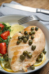 Delicious cooked chicken fillet with capers and salad served on table, closeup