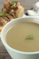 Cup of delicious homemade bone broth on grey wooden table, closeup