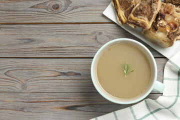 Cup of delicious homemade broth and bones on grey wooden table, flat lay. Space for text