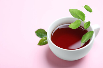 Fresh sage leaves falling into cup of freshly brewed tea on pink background, space for text