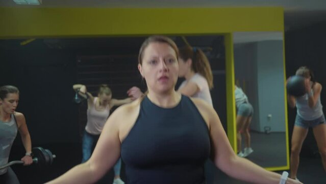 Close up shot of a chubby Caucasian woman skipping a rope at the gym. Female fitness group celebrating successful tabata workout, happily applauding.