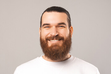 Obraz premium Close up portrait of a young smiling bearded man looking at the camera. Studio shot over grey background.