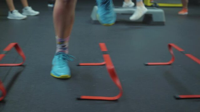 Close-up shot of fit Caucasian girl doing a workout with speed training hurdles at the very crowded ladies� gym.