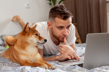young man uses laptop while lying next to shiba inu dog 