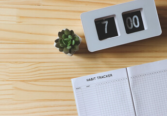flat lay of habit tracker book, flip clock 7 am and succulent plant pot on wooden table background...