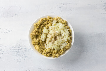 White bowl with soaked ground green lentils, onions and spices on a light blue background. Cooking healthy vegan food, toppings for vegan dumplings or cutlets