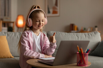 Little Schoolgirl Using Laptop Gesturing Thumbs Up Sitting At Home