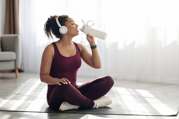 Athletic black woman drinking water while exercising