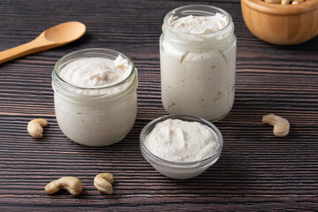 Vegetarian cream cheese made from fermented cashews; in glass jars on dark wooden background.