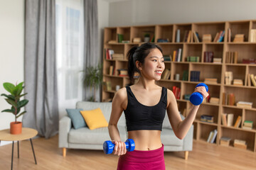 Fototapeta na wymiar Slim young korean woman lifting up dumbbells having training at home, taking care of body in the morning