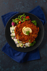 Classic, traditional Viennese sirloin schnitzel. Served on potato salad. Breaded. Dark background.