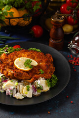 Classic, traditional Viennese sirloin schnitzel. Served on potato salad. Breaded. Dark background.